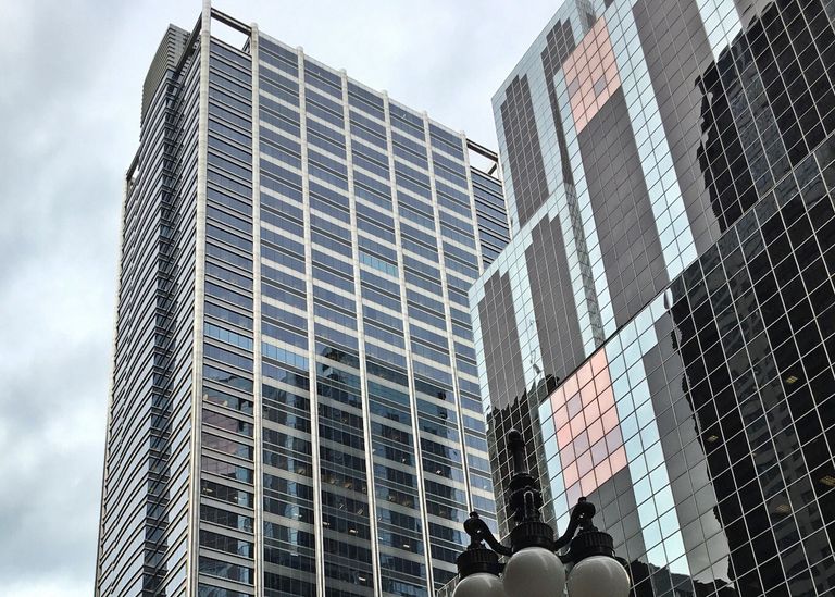 Tall modern skyscrapers with reflective glass facades against a cloudy sky, featuring a street lamp in the foreground.