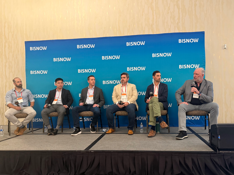 Six men sit on a panel stage with microphones, in front of a "BISNOW" backdrop.