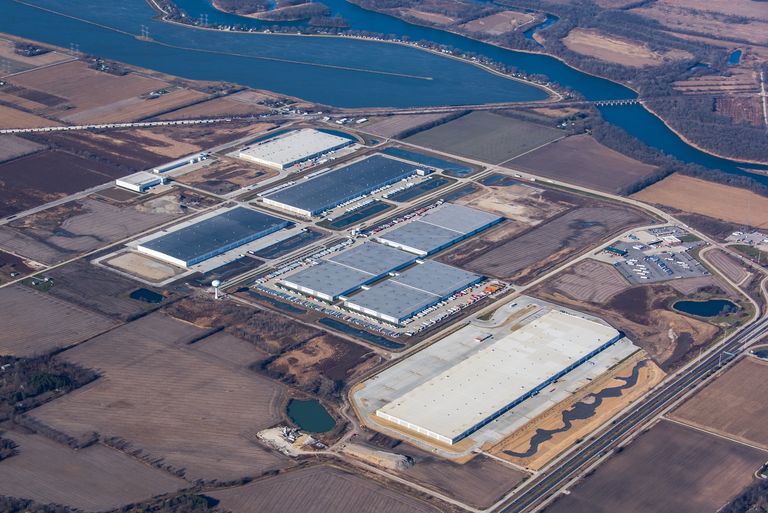 Aerial view of an industrial park with large warehouses surrounded by farmland and a river in the background.