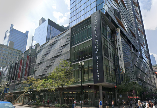 A modern multi-story glass and steel building, Block Thirty Seven, featuring retail and dining spaces, is located on a bustling city street.