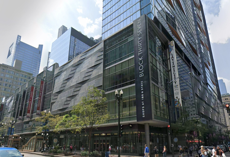 A modern multi-story glass and steel building, Block Thirty Seven, featuring retail and dining spaces, is located on a bustling city street.