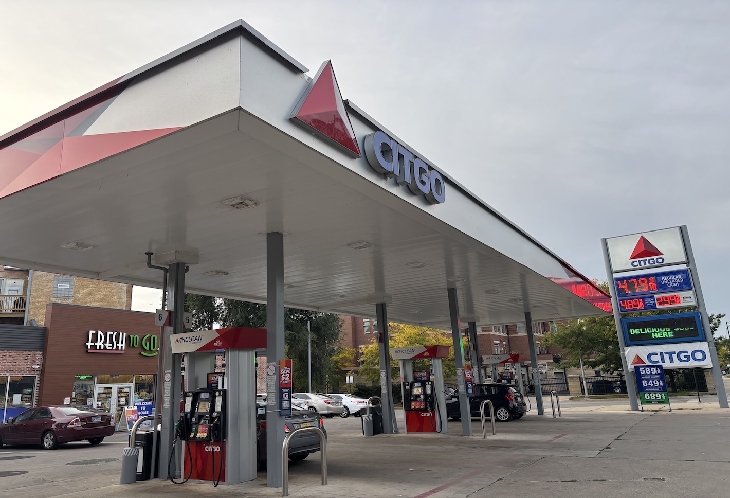 Gas station with Citgo signage, multiple fuel pumps, and a price sign displaying fuel costs. Cars are parked by the pumps, and a store is nearby.