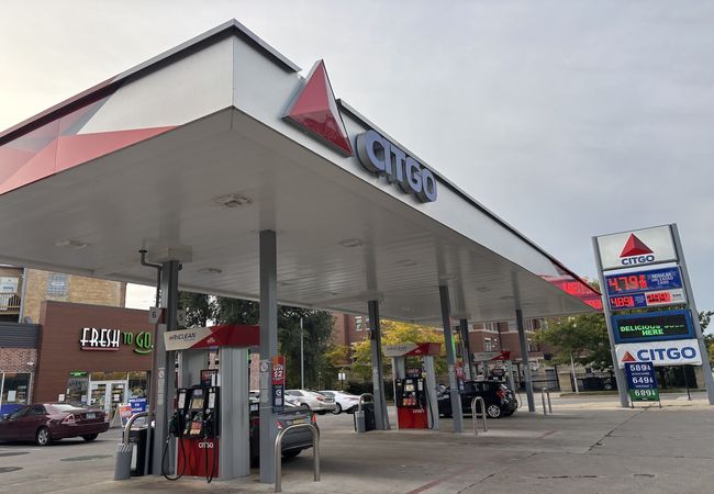 Gas station with Citgo signage, multiple fuel pumps, and a price sign displaying fuel costs. Cars are parked by the pumps, and a store is nearby.