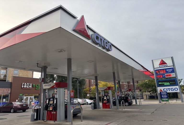 Gas station with Citgo signage, multiple fuel pumps, and a price sign displaying fuel costs. Cars are parked by the pumps, and a store is nearby.