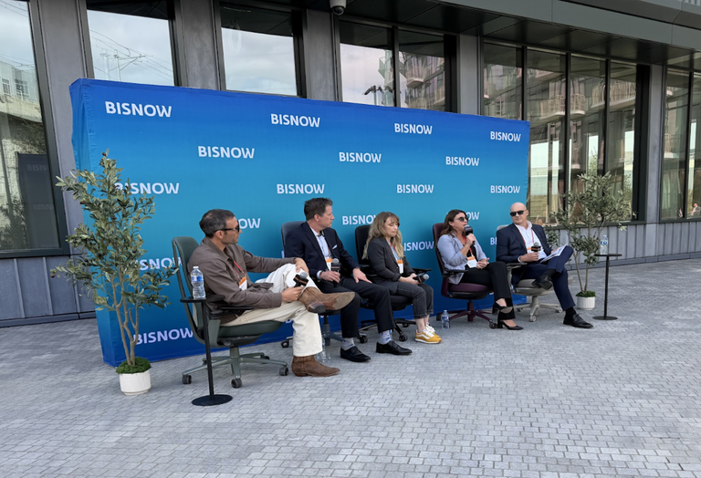 Five people, three men and two women, sitting on a discussion panel with microphones in front of a blue Bisnow backdrop.