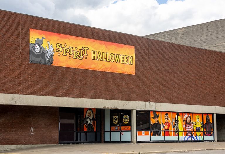 Brick building with a large "Spirit Halloween" banner and decorated windows showing costume designs including a witch, clown, and robot.