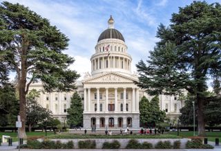 A photo of the state capitol of California, a Neoclassical building with a green lawn in front.