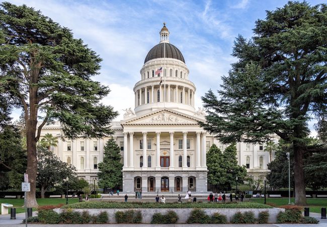 A photo of the state capitol of California, a Neoclassical building with a green lawn in front.