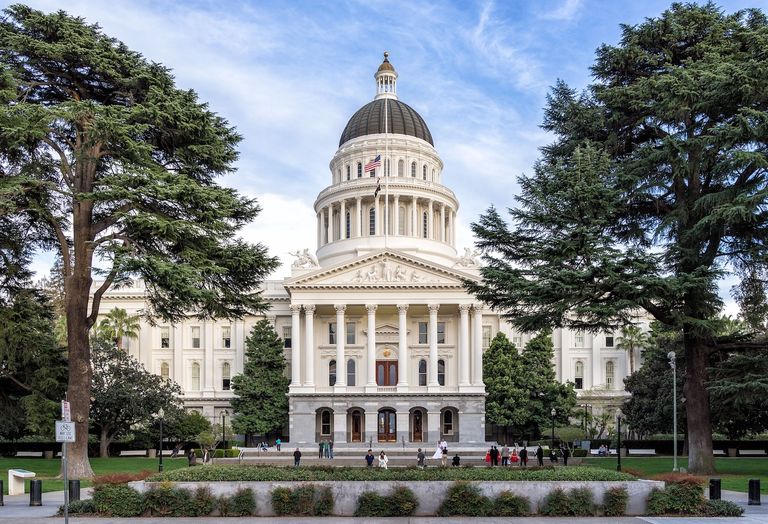 A photo of the state capitol of California, a Neoclassical building with a green lawn in front.