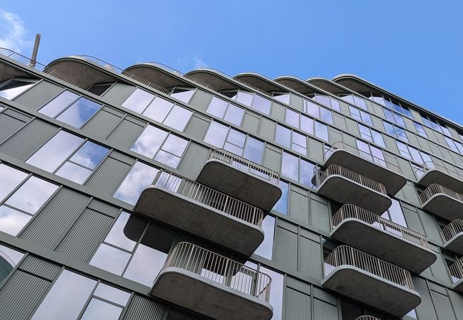 Modern building with staggered balconies and large windows under a clear blue sky.