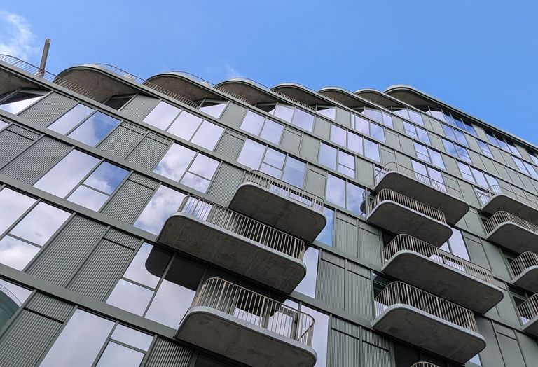 Modern building with staggered balconies and large windows under a clear blue sky.