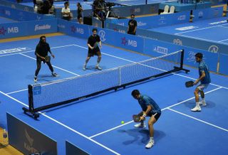 Pickleball players await a return shot at an indoor venue.