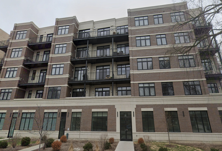A five-story brown brick building with black framed windows and balconies on certain levels; entrance marked with 1555 above the door.