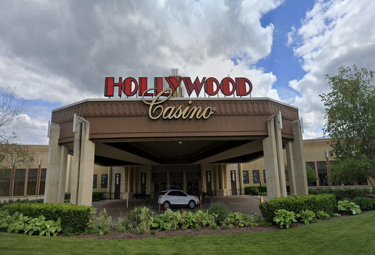 Entrance of Hollywood Casino with red and gold sign, surrounded by landscaping, under a cloudy sky.