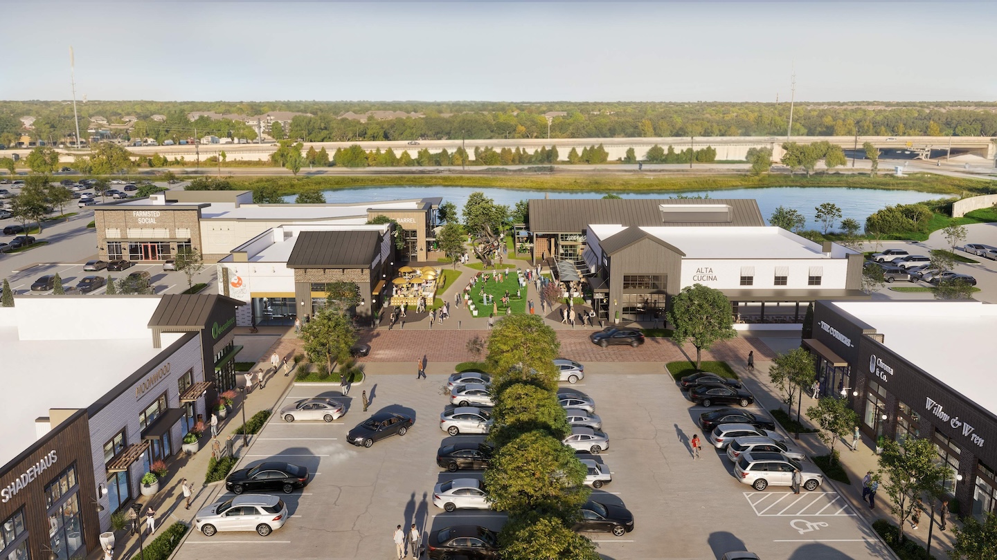 Aerial view of a shopping center with various shops, restaurants, and a central grassy area. Cars are parked in the lot, and people walk around.