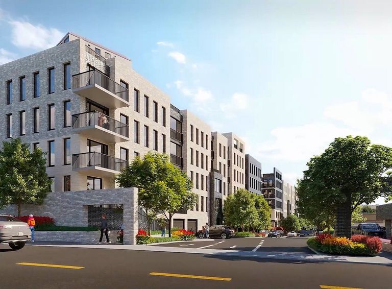 Modern apartment building with balconies, trees, and a sidewalk along a road under a clear blue sky.