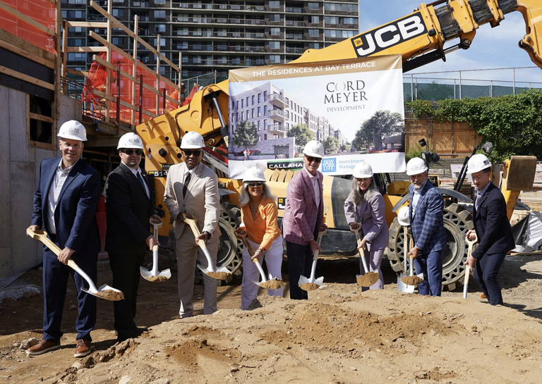 Eight people in hard hats hold shovels during a groundbreaking ceremony in front of construction machinery and a banner for Cord Meyer Development.