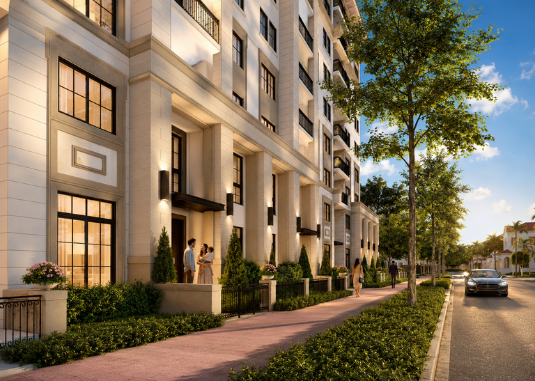 Elegant residential building with balconies, lush greenery, and people walking on a sunlit sidewalk. A car is parked on the street.