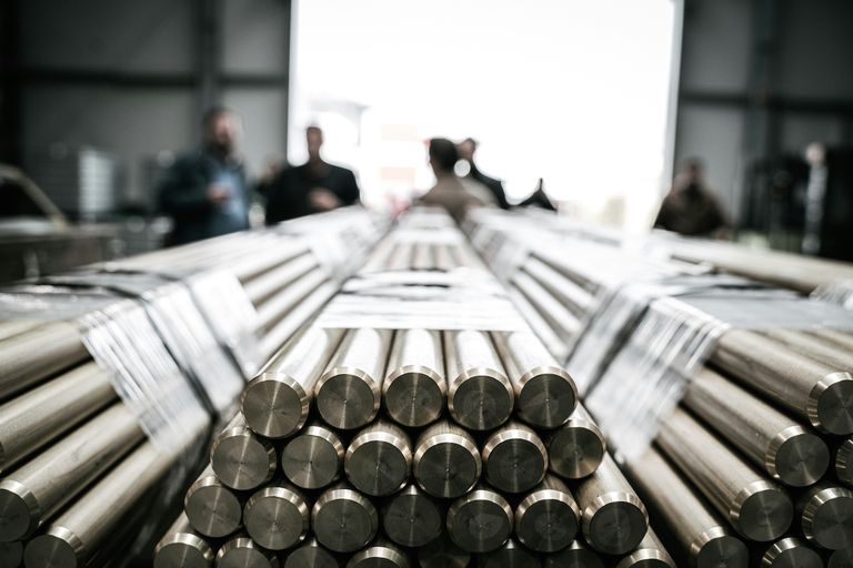 A stack of metallic rods in a warehouse, with people blurred in the background.