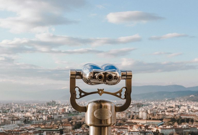 A binocular telescope overlooking a cityscape with partly cloudy skies and distant mountains.