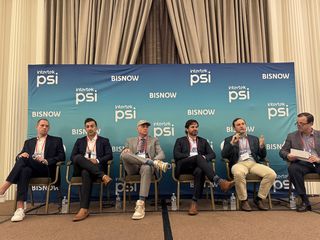 Six men sitting on a panel stage with a blue backdrop featuring logos of "Intertek PSI" and "BISNOW", engaged in a discussion.