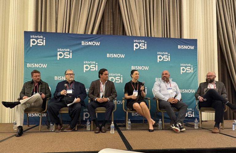 Six people sit on stage with microphones at a panel discussion, against a backdrop with "Intertek PSI" and "BISNOW" logos.