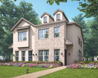 A modern two-story cottage with brick and stucco facade, surrounded by colorful flower beds and lush green trees under a clear blue sky.