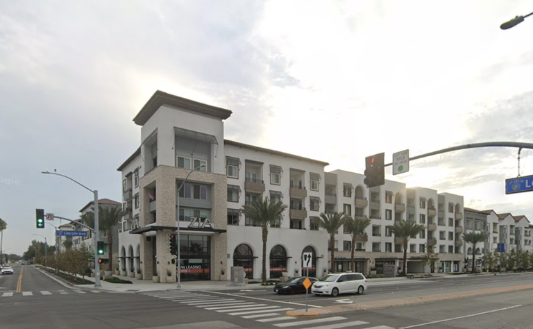 Street corner with modern multi-story building and palm trees, featuring shops and a leasing office below, under a bright, cloudy sky.