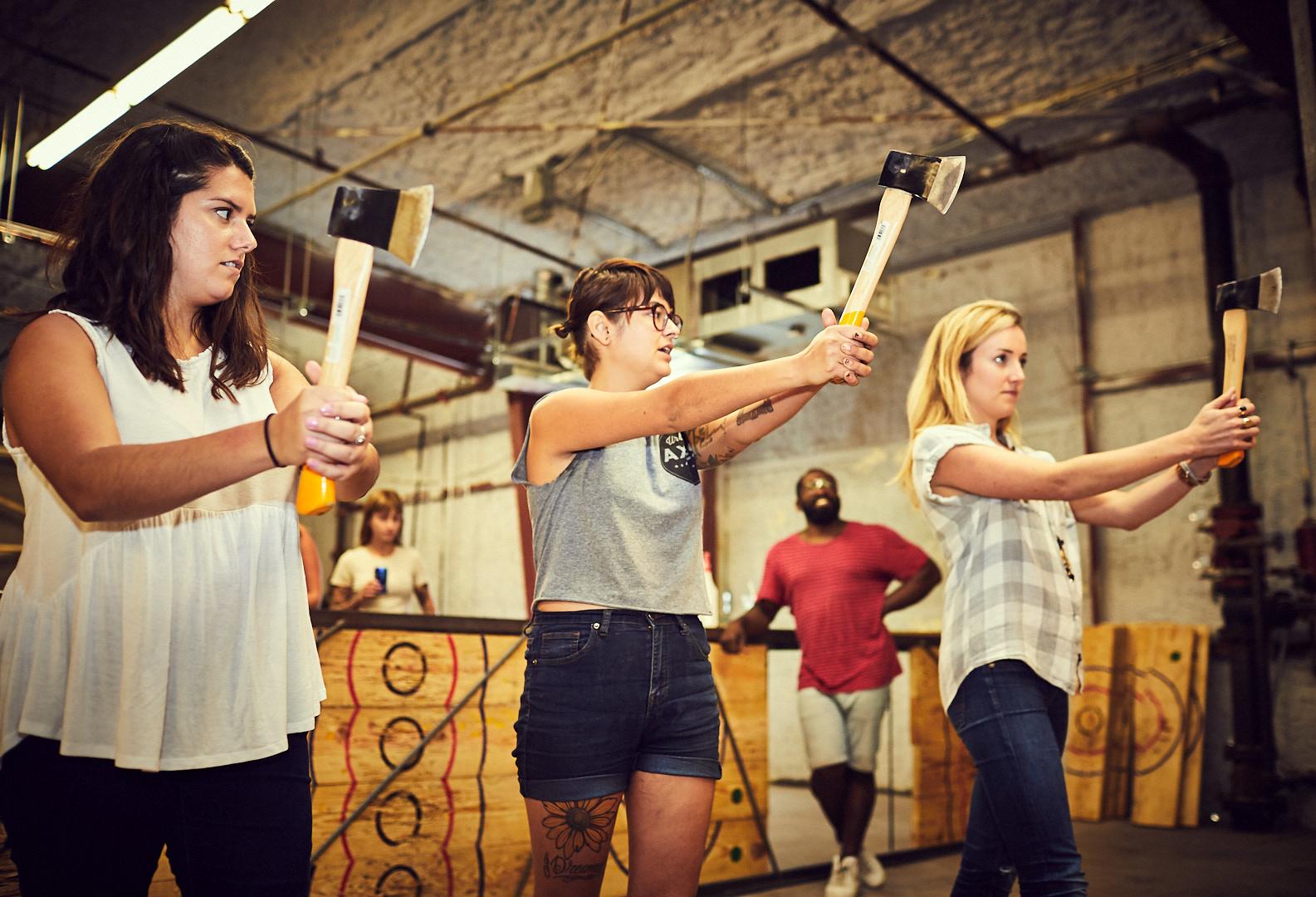 An Urban Axes coach (middle) teaches two new participants ax-throwing form.