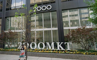 Exterior view of a modern office building with the number "2000" and "2000MKT" displayed. People walk by on the sidewalk.