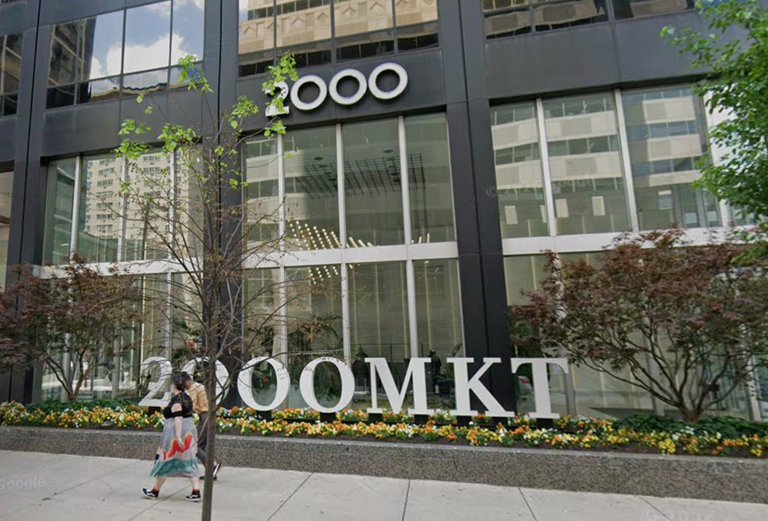 Exterior view of a modern office building with the number "2000" and "2000MKT" displayed. People walk by on the sidewalk.