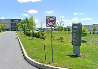 Driveway leading to a distribution center with signs prohibiting trucks and guiding to entrances, surrounded by green lawns.