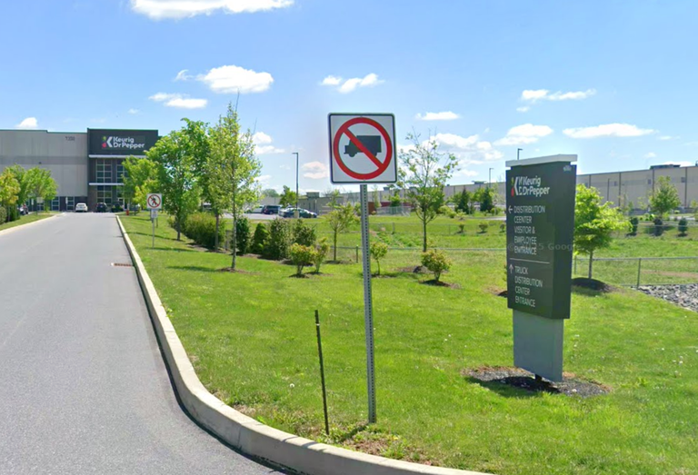 Driveway leading to a distribution center with signs prohibiting trucks and guiding to entrances, surrounded by green lawns.