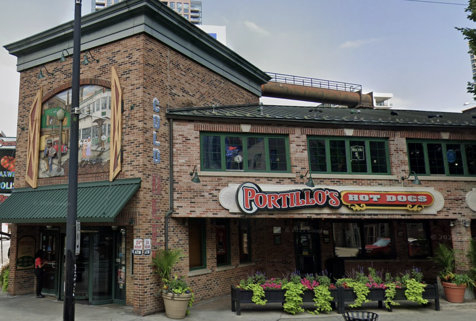 A brick building with a Portillo's Hot Dogs sign, green awnings, and colorful window boxes.