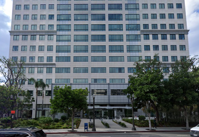 A tall, modern office building with a symmetrical facade and glass windows, surrounded by trees. Large numbers "655" are in front of it.