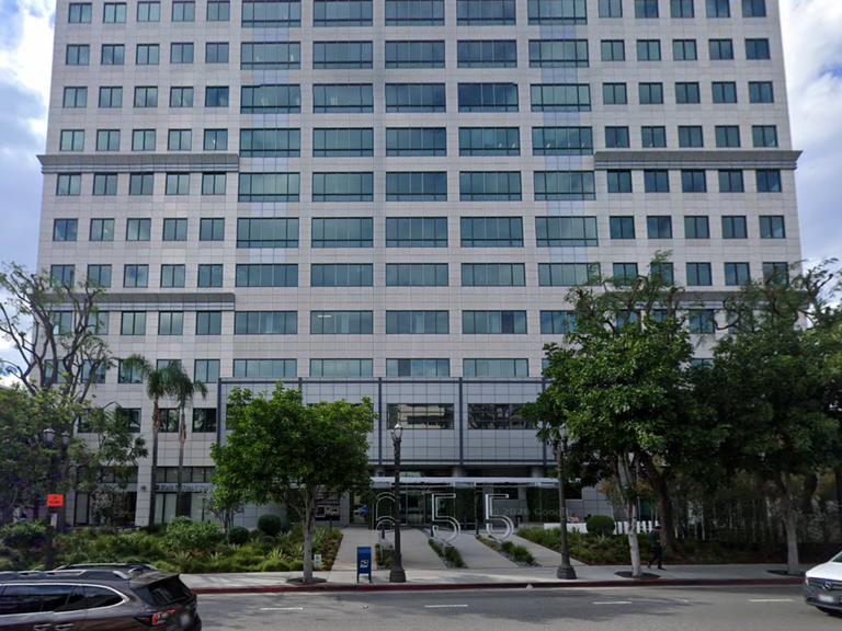A tall, modern office building with a symmetrical facade and glass windows, surrounded by trees.