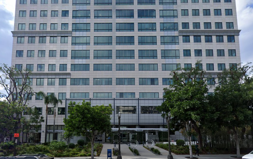A tall, modern office building with a symmetrical facade and glass windows, surrounded by trees. Large numbers "655" are in front of it.