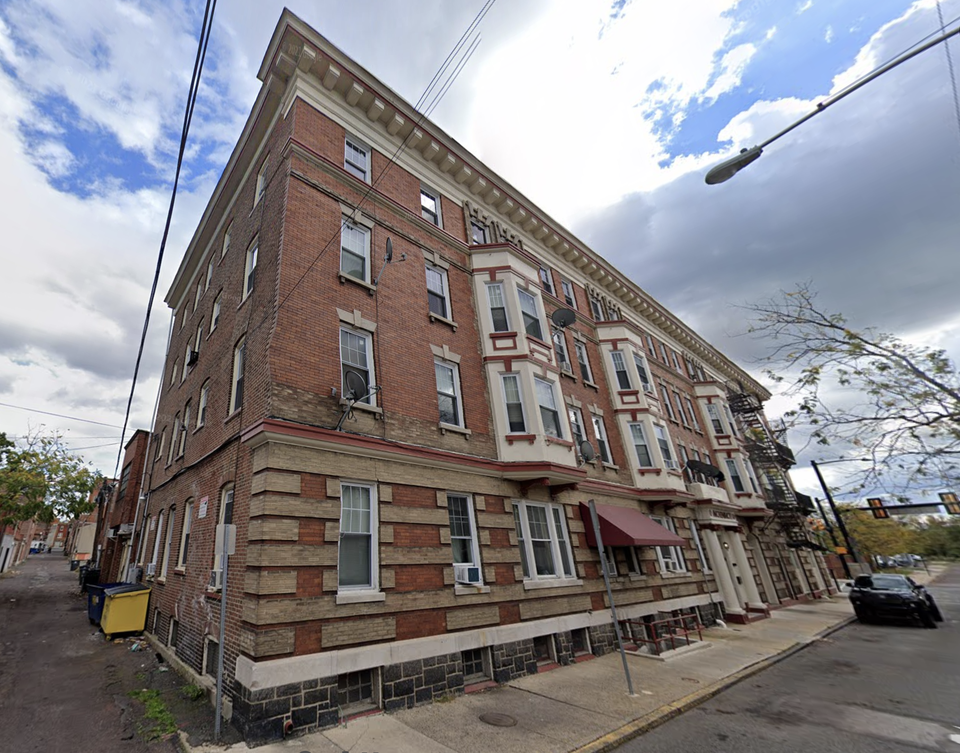 A four-story brick apartment building with ornate details on a city street corner under a cloudy sky.