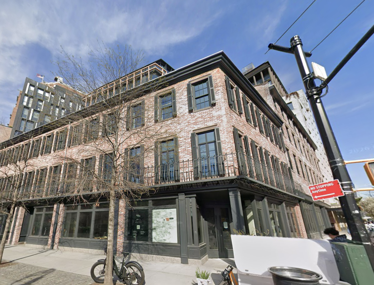 Three-story brick building with large windows and a bike parked outside, set on an urban street corner under a blue sky.