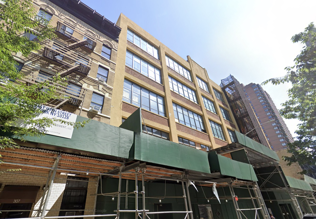 Street view of a mid-rise building with fire escapes and green construction scaffolding in an urban area, under a clear sky.
