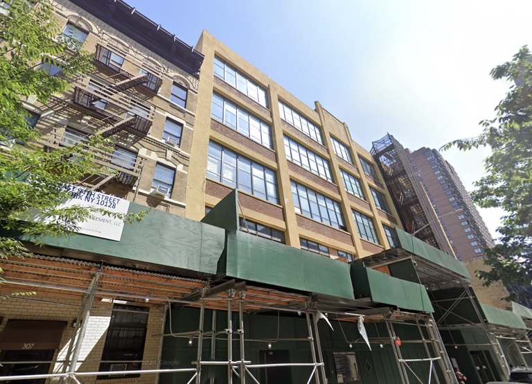 Street view of a mid-rise building with fire escapes and green construction scaffolding in an urban area, under a clear sky.