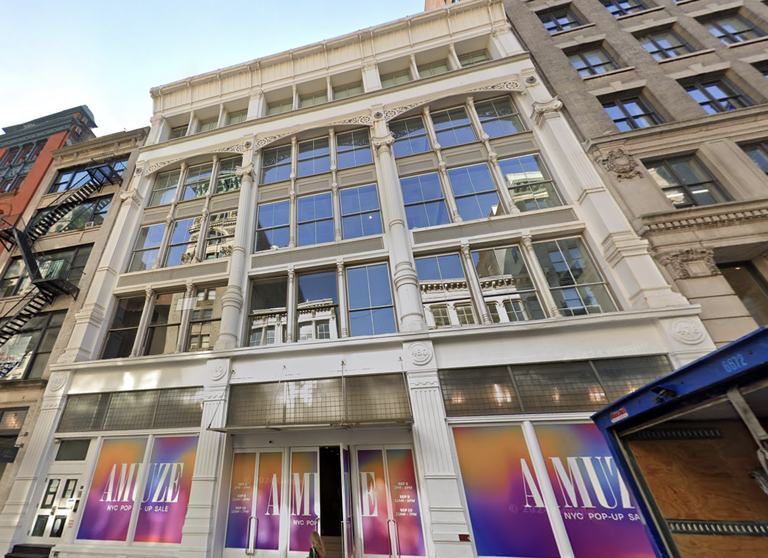 Storefront with large windows and columns, featuring "AMUZE" pop-up sale signage in vibrant colors. Urban building facade in a city setting.