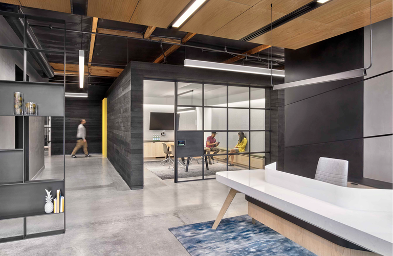 Modern office with a glass-walled meeting room, people sitting inside, and a sleek reception area with minimalist decor outside.