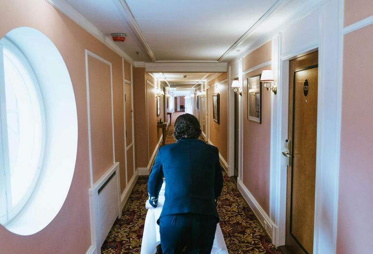 A bellhop delivering room service in the hallway of a hotel