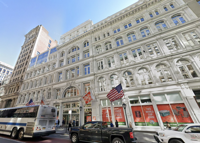 Large white multi-story building with arched windows, American flags, vehicles, and pedestrians on the street in front.