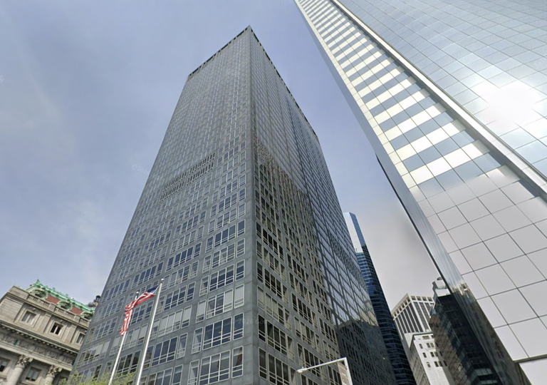 Tall office buildings with glass and metal facades under a cloudy sky, one displaying a U.S. flag at street level.