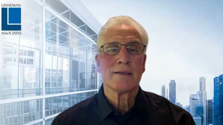 Man in glasses with light hair against a modern cityscape background, with "Linneman Associates" logo in the top left corner.