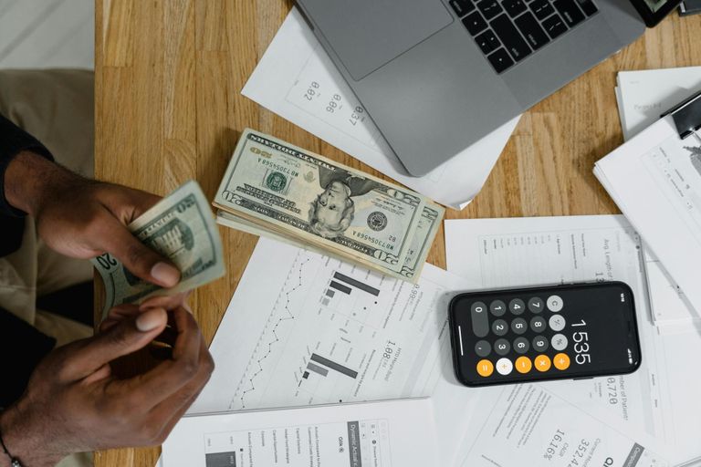 Person counting cash while using a calculator phone app.