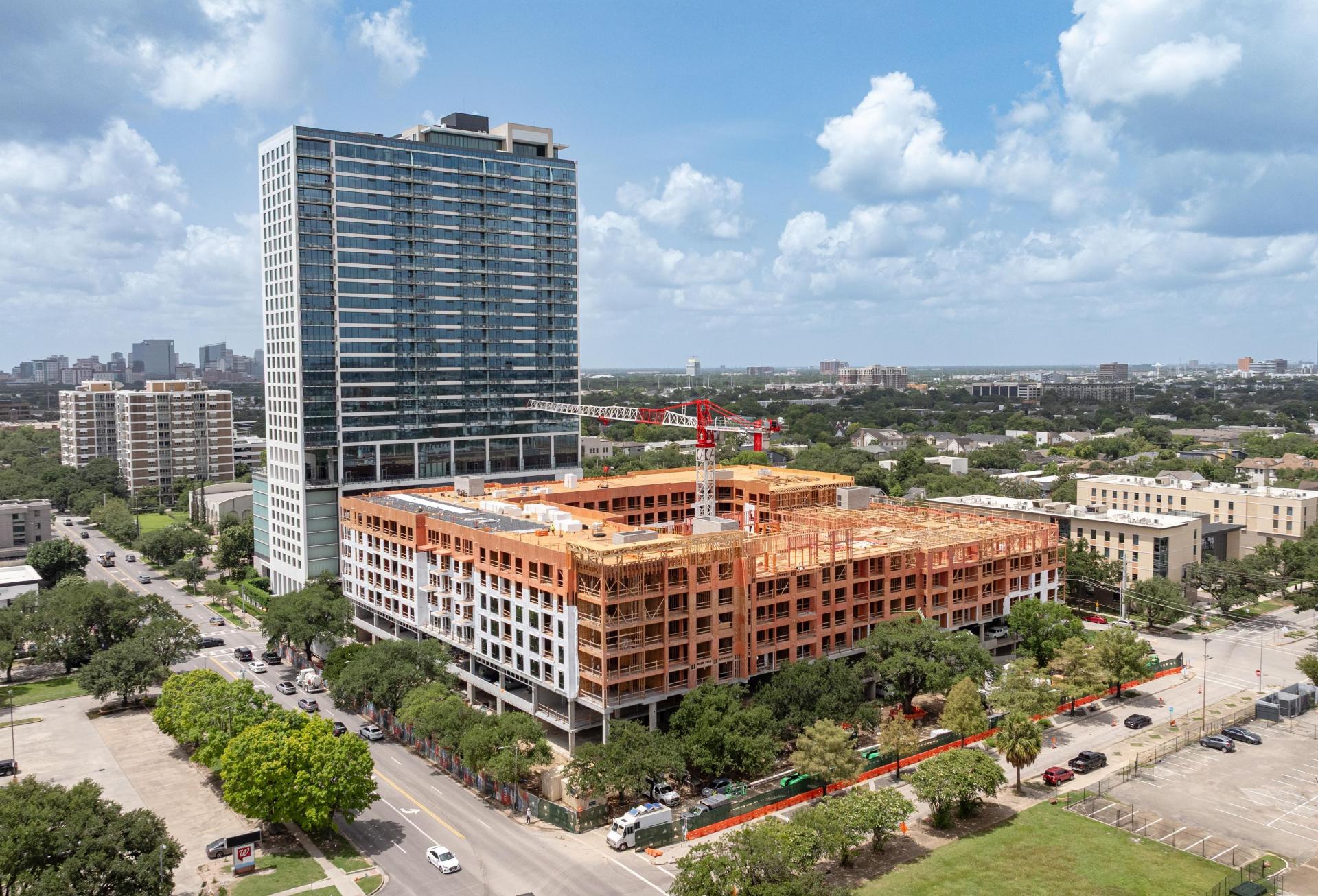 A seven-story building under construction with a crane in the center in front of a high-rise, taken from above