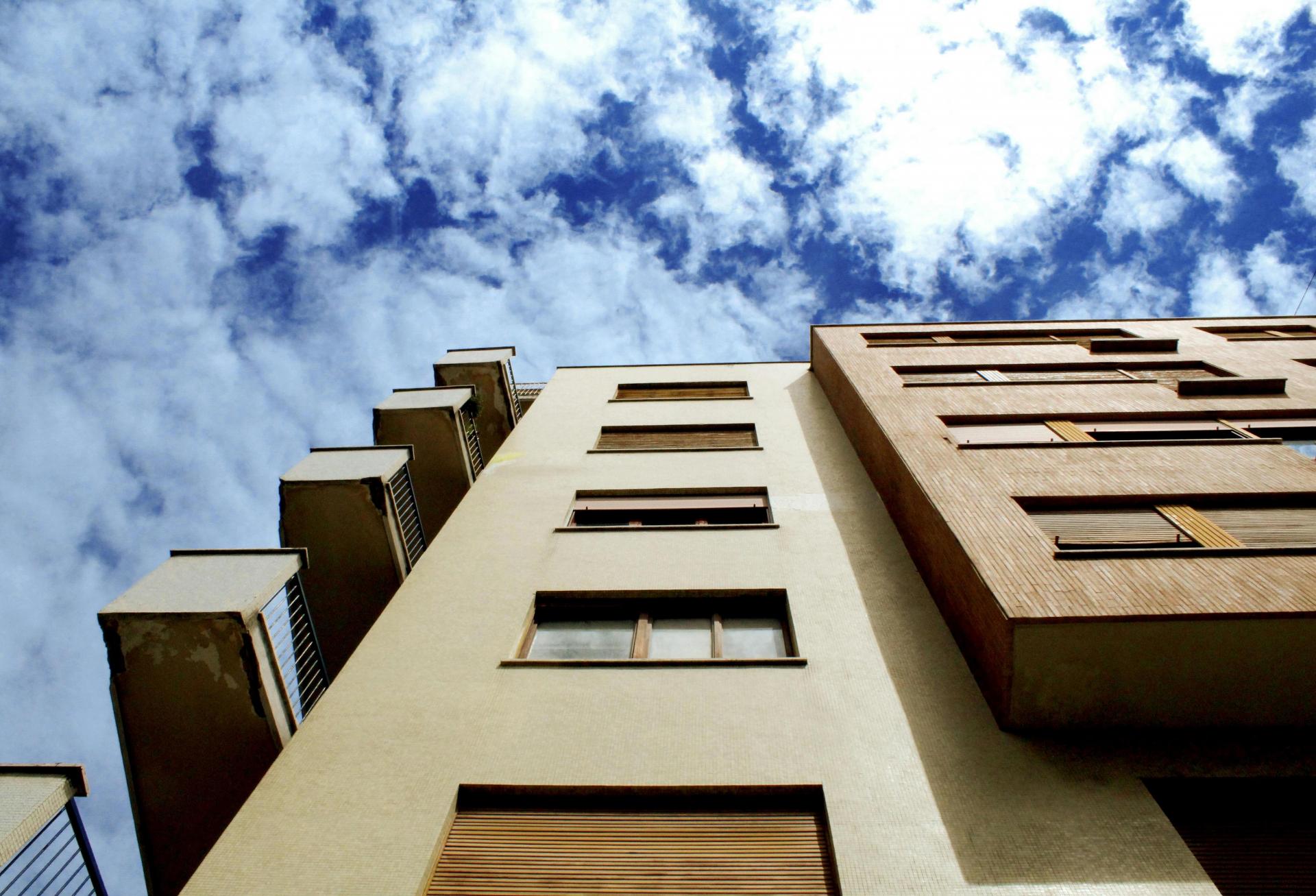 exterior of an apartment building facing up toward a sunny sky with white clouds